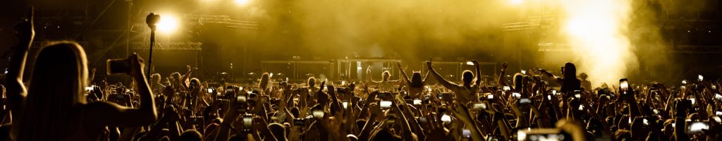 Rear view of excited fans having fun at music festival and taking pictures of stage with their smart phones.  Copy space.